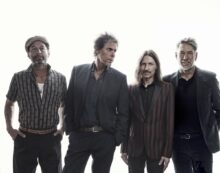 The Whitlams performing with a large orchestra, including strings and brass, led by a conductor.