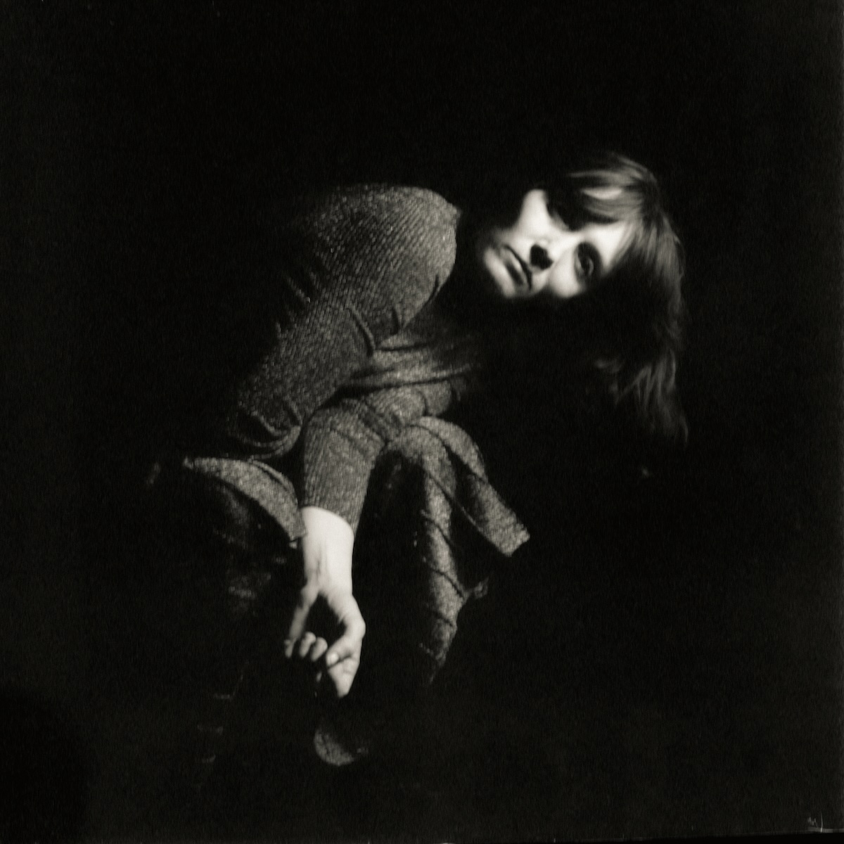 Sarah Blasko performing live, acoustic guitar in hand, stage lighting illuminating her face